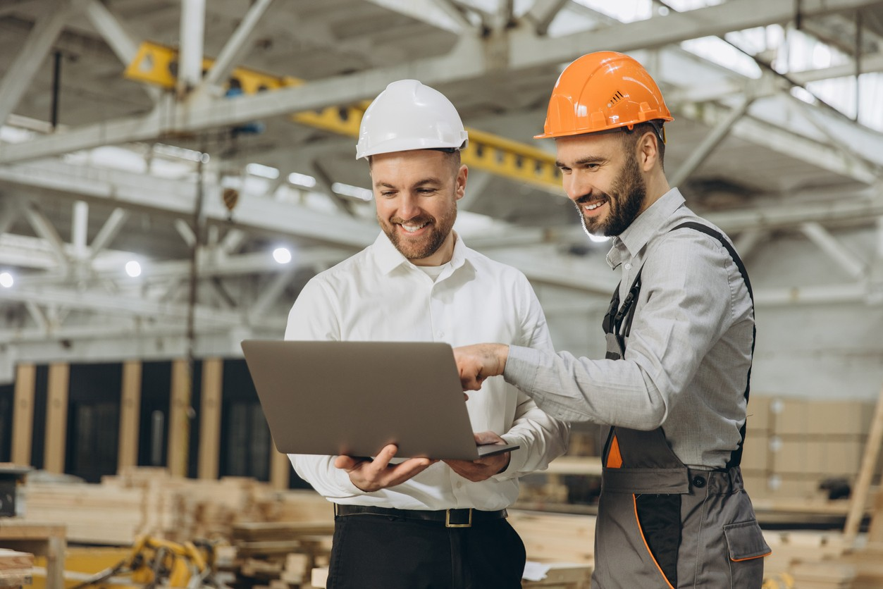 Twee medewerkers in een fabriek bekijken gezamenlijk informatie op een laptop