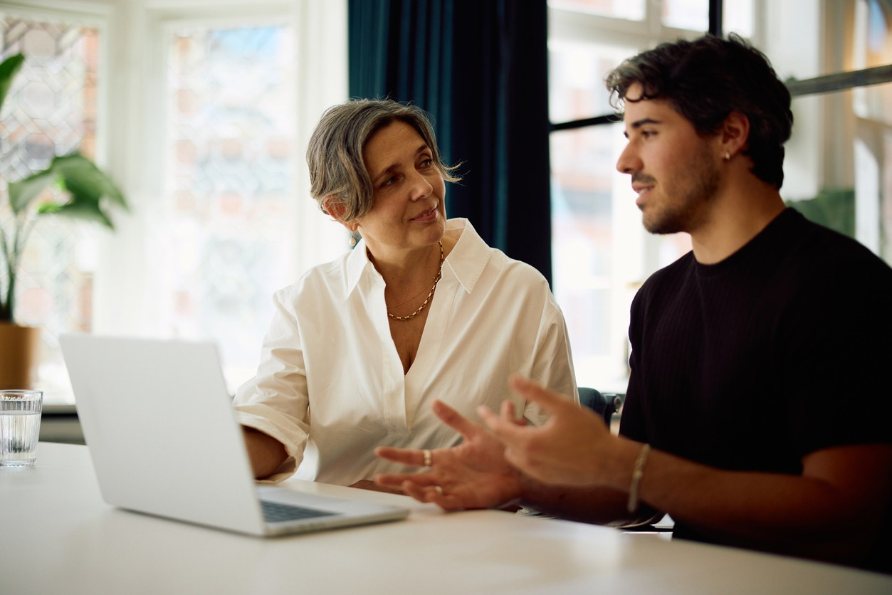 Twee collega's bespreken informatie aan een laptop aan een witte tafel